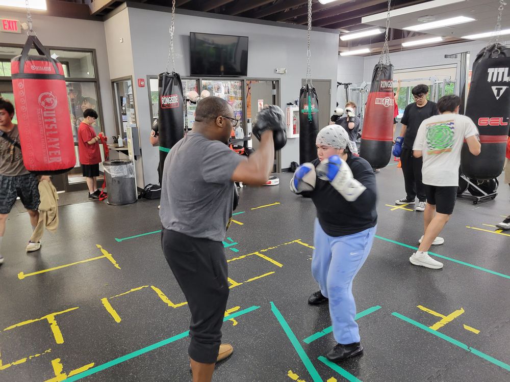 A coach holding focus mitts for a boxer on the training floor